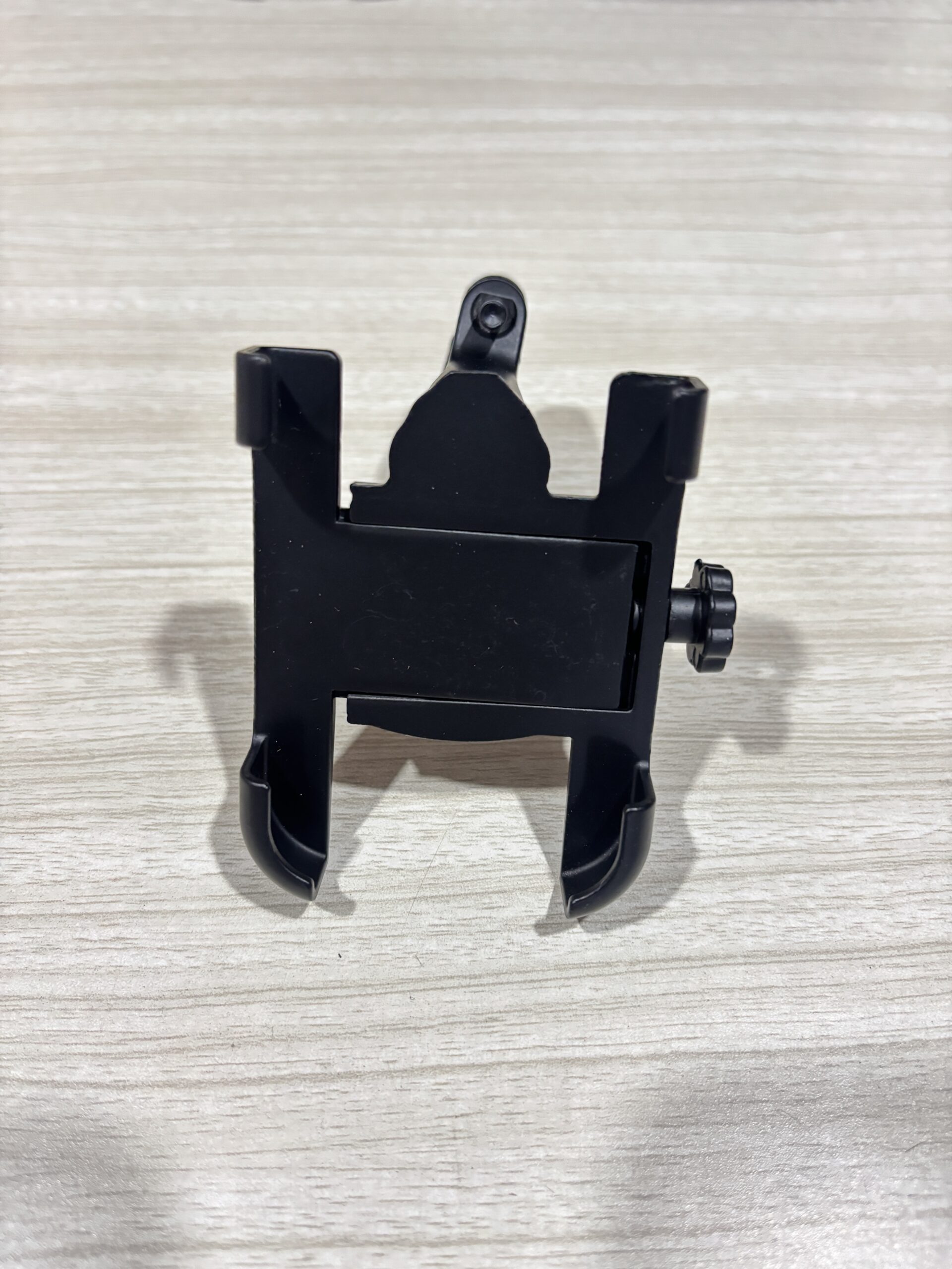 IMG_6407 - laxmiautocare.com Black plastic mounting bracket with two side clamps on a light wood surface, likely a camera or accessory mount
