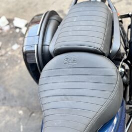 Close-up of a gray ribbed leather motorcycle seat with an embossed logo and a backrest above it