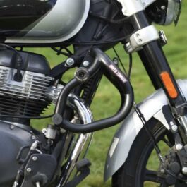Close-up of a Royal Enfield motorcycle showing the engine, black exhaust pipe, and front fork with an orange reflector on a green background.