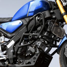 Blue Yamaha motorcycle close-up showing the fuel tank, engine, black crash bars, radiator guard, and gold front suspension