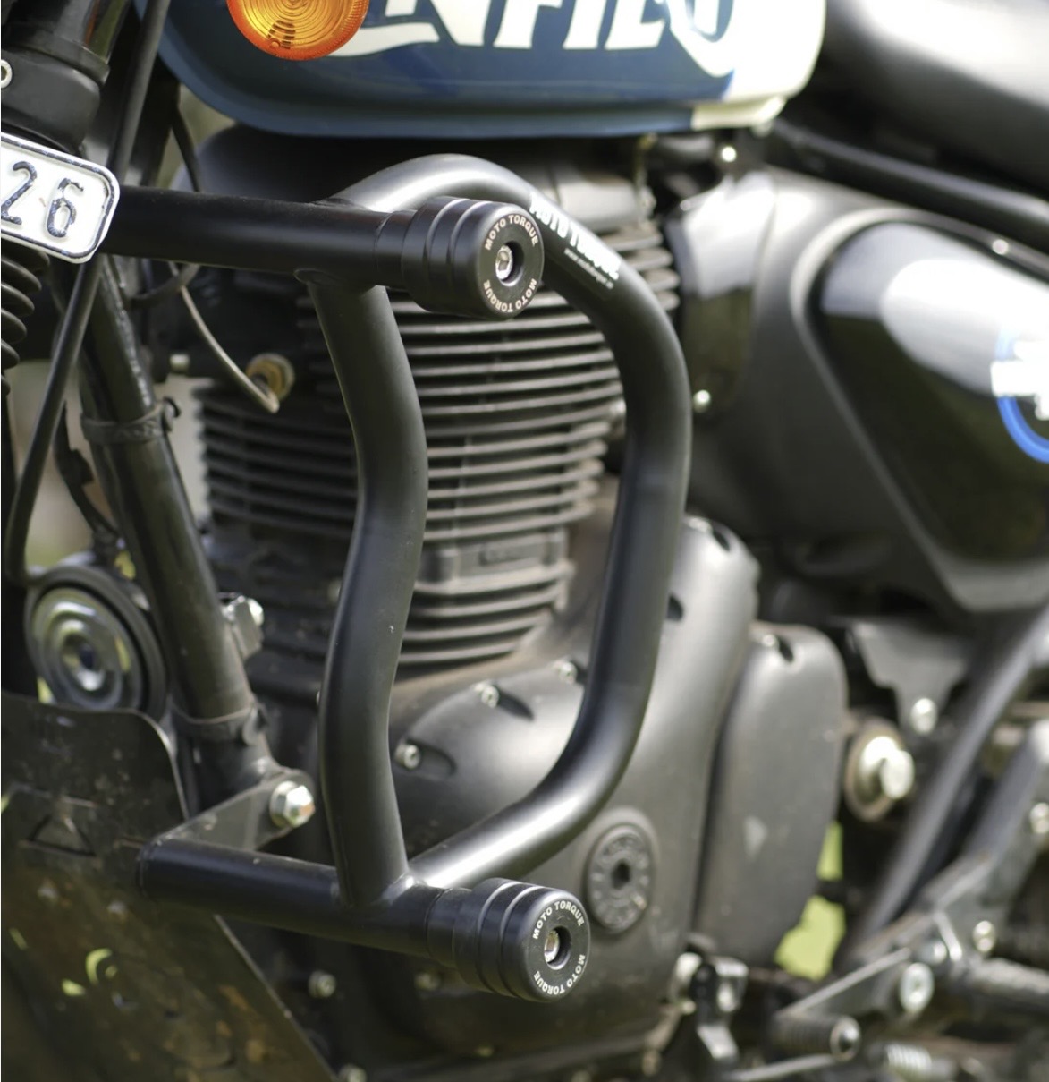 Screenshot - laxmiautocare.com Close-up of a motorcycle engine with black tubular crash bars and small caps labeled 'Moto Torque' for protection.
