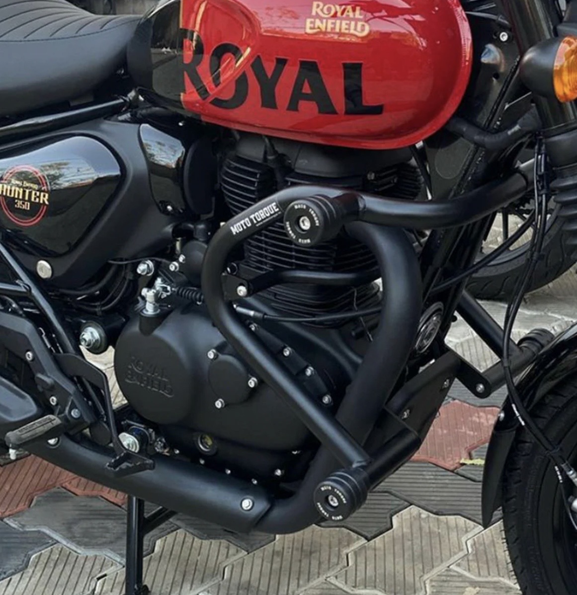 Close-up of a Royal Enfield Hunter 350 motorcycle with a red fuel tank and black engine guard.