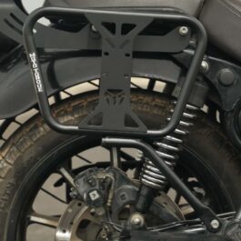 Screenshot - laxmiautocare.com Black metal rectangular motorcycle rear luggage rack mounted over the rear wheel, with a visible coil spring suspension and brake disc beside it.