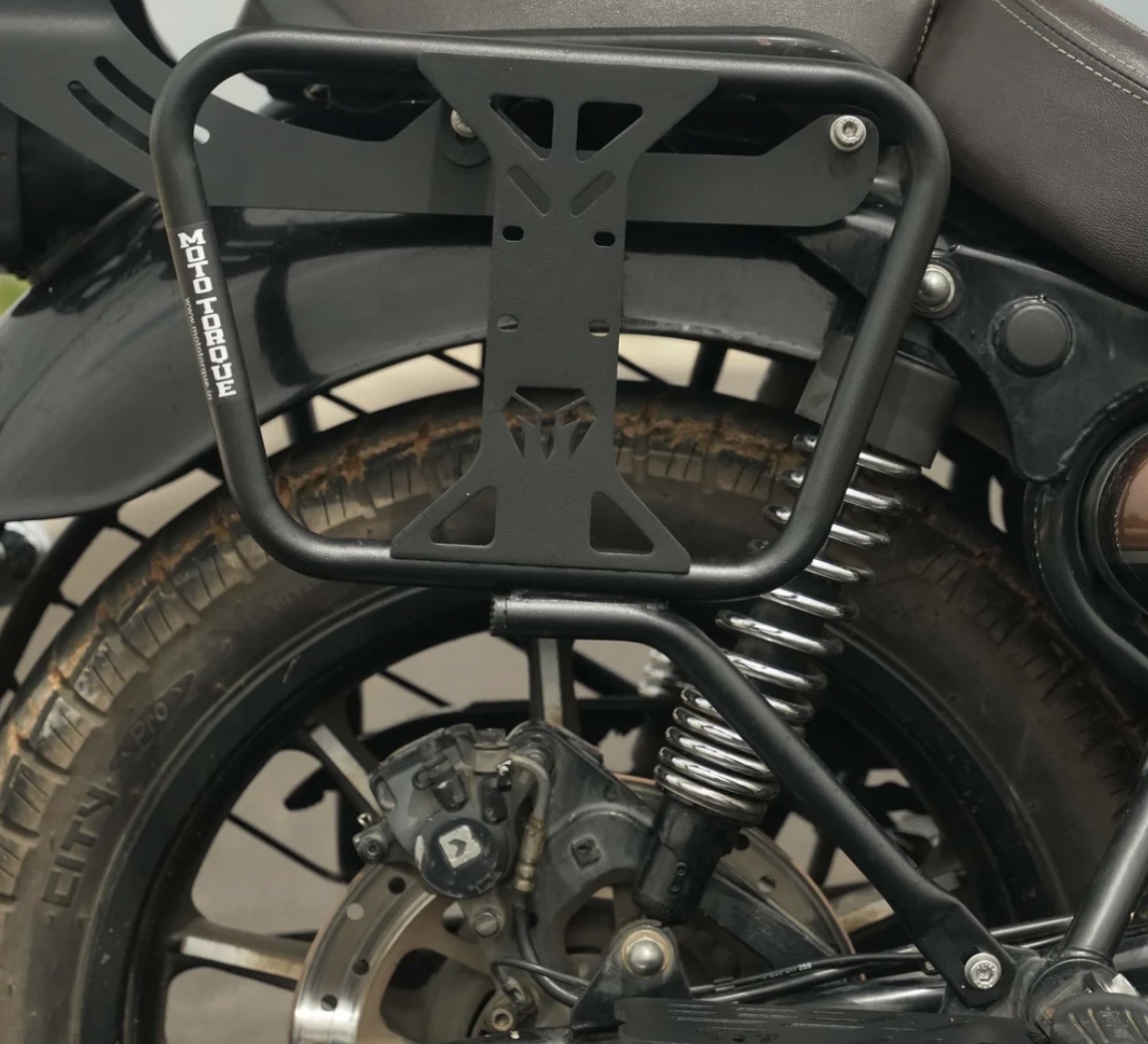Black metal rectangular motorcycle rear luggage rack mounted over the rear wheel, with a visible coil spring suspension and brake disc beside it.