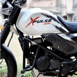 Screenshot - laxmiautocare.com Close-up of a white motorcycle fuel tank with red 'XPulse 200' branding and black graphic streaks; engine and frame visible below.