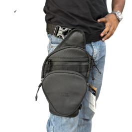 Man wearing a black rounded hip bag attached to a tactical belt at the waist, with one hand on his hip and a silver wristwatch visible.