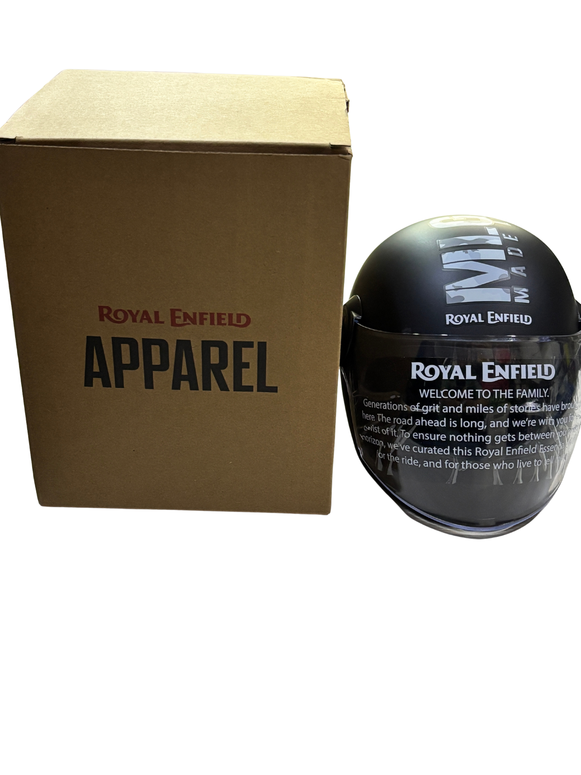f1dff656-e580-484d-9e46-712d70c9c140 - laxmiautocare.com Brown cardboard Royal Enfield Apparel box next to a black glossy Royal Enfield helmet with white logo on a black background.