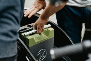 Close-up of hands handling a green car battery in the trunk of a vehicle, preparing to install or remove it.