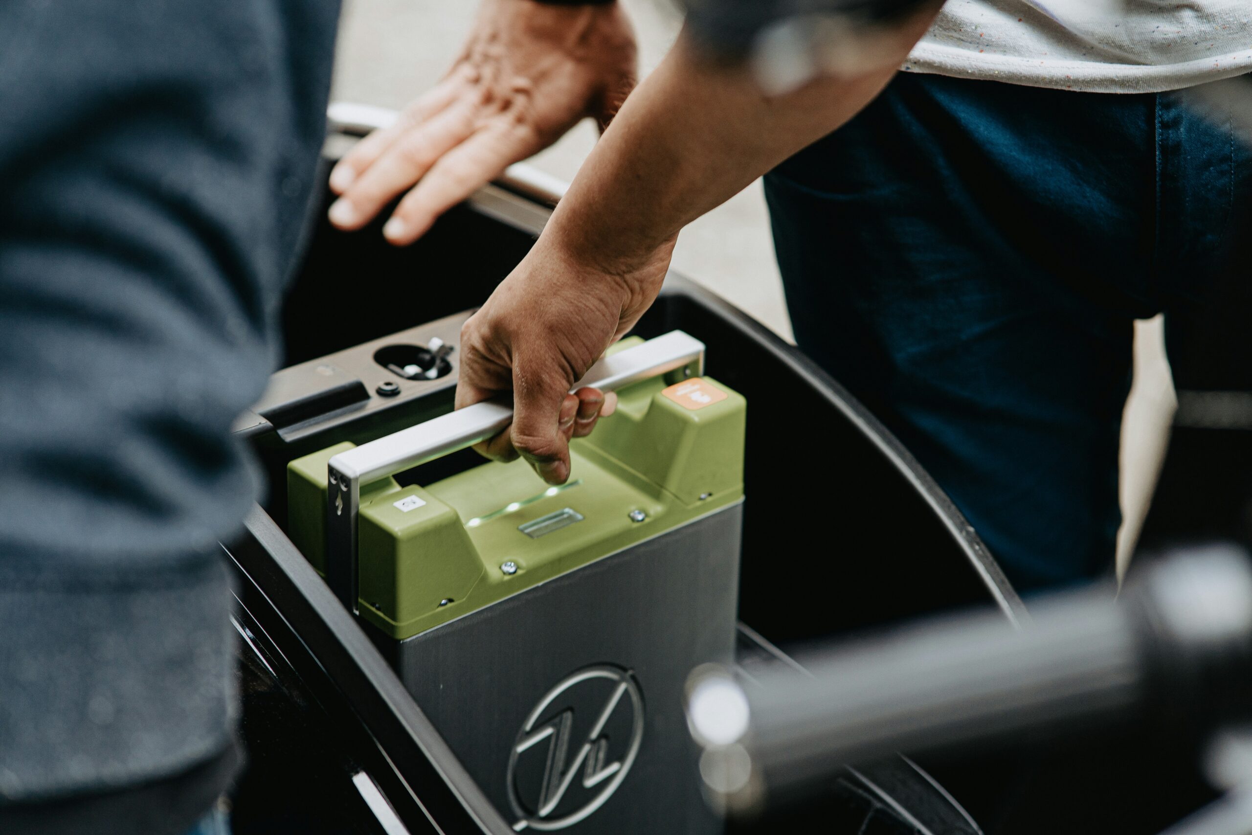 Close-up of hands handling a green car battery in the trunk of a vehicle, preparing to install or remove it.