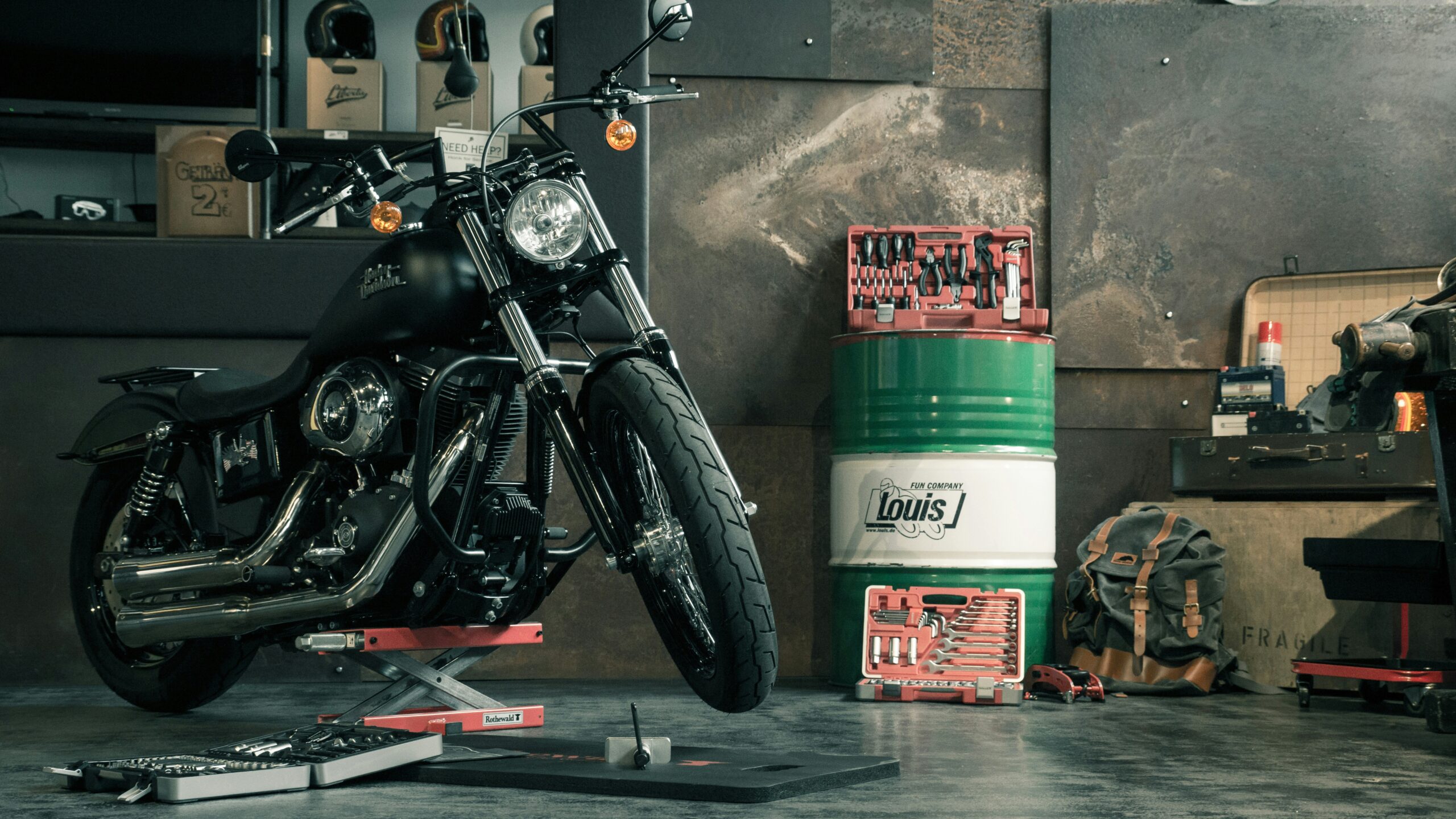 Black motorcycle on a lift in a cluttered workshop with helmets and boxes in the background