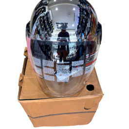 41993704-02c4-45b0-b9ae-32efb3c6db5c - laxmiautocare.com Chrome, full-face motorcycle helmet with a highly reflective visor, placed on a cardboard box; store shelves and lights reflected in the visor surface.