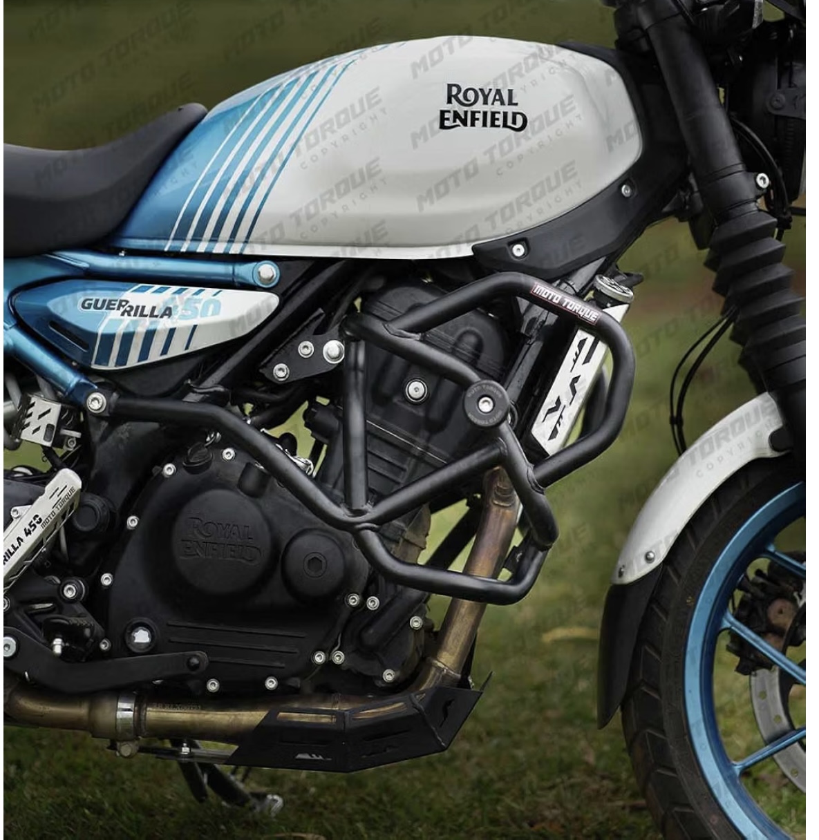 Screenshot - laxmiautocare.com Close-up of a Royal Enfield motorcycle with a blue-and-white fuel tank bearing the Royal Enfield logo, engine guard, and blue front wheel.