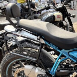 Close-up of a Royal Enfield motorcycle’s fuel tank and rear wheel, with a visible front disc brake and surrounding bikes in the background