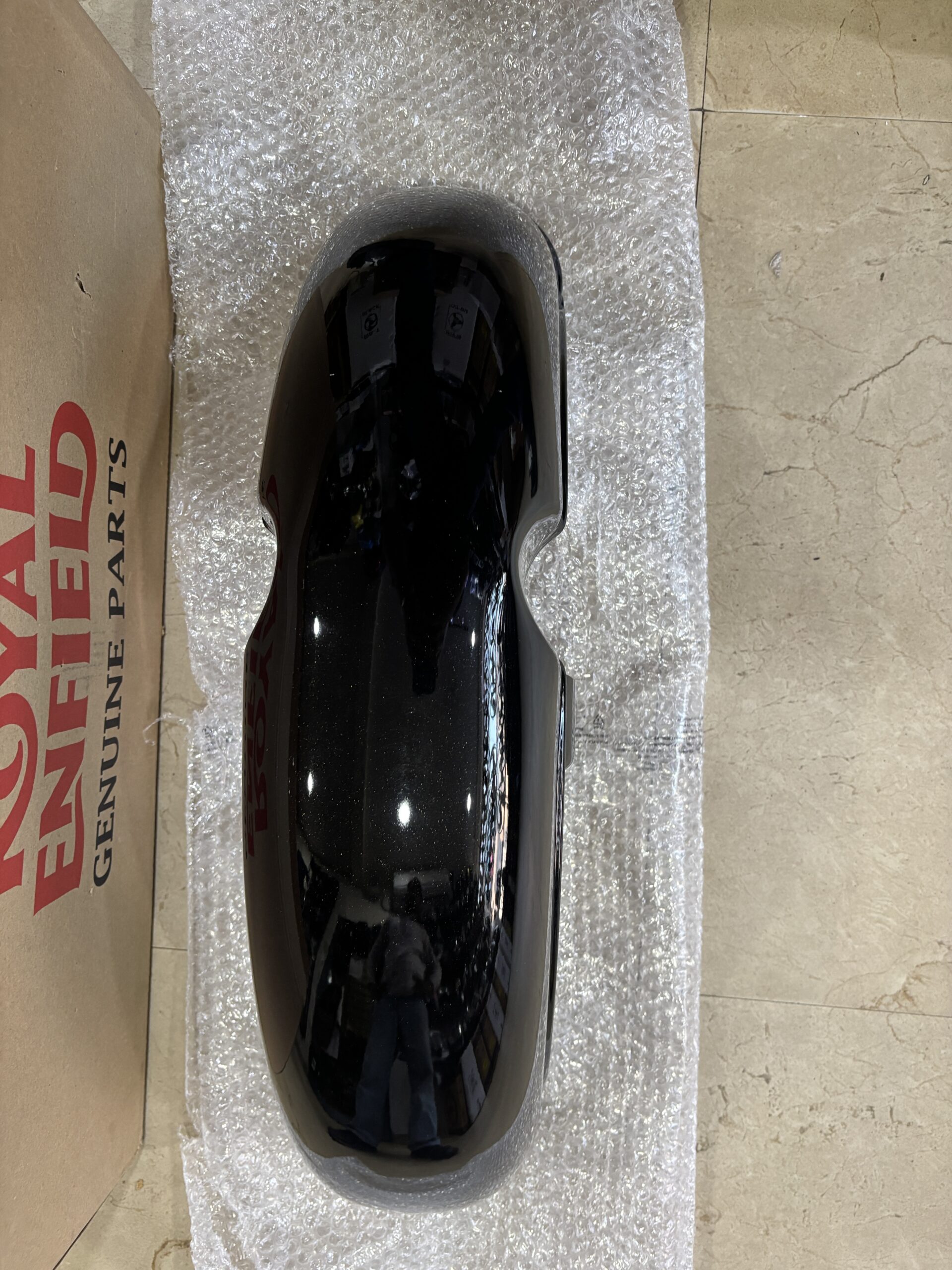 IMG_6710 - laxmiautocare.com Shiny black automotive panel (likely a fuel tank or fender) lying on bubble wrap beside a cardboard box on a tiled floor